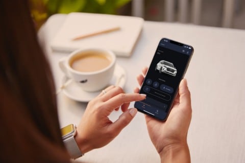 Un teléfono donde se ve la aplicación Lincoln Way. También se ve un auto lincoln de fondo que está en una playa.